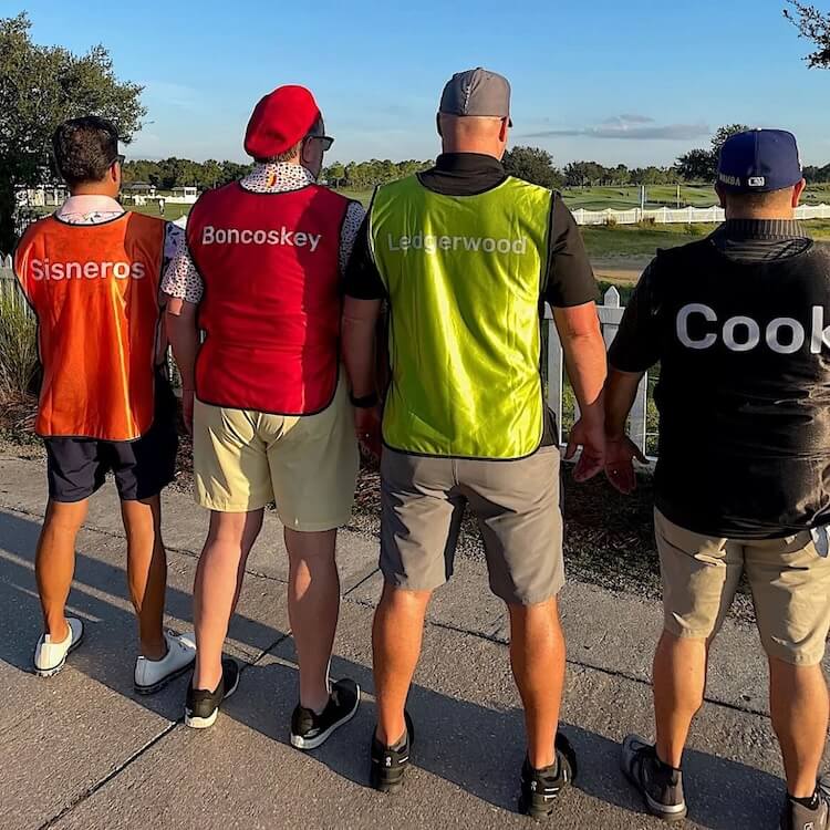 Four men standing outdoors, wearing colored vests with names printed on them.