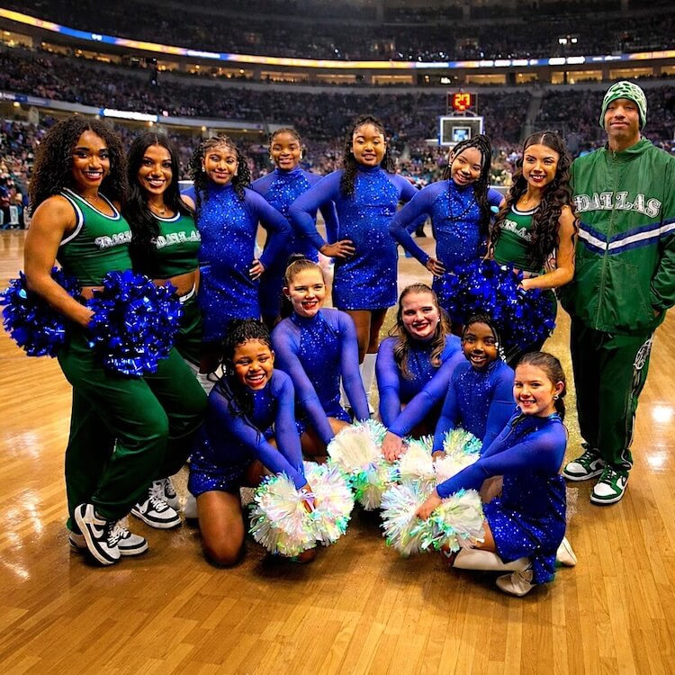Cheerleaders wearing blue and green uniforms holding metallic and iridescent pom poms on a basketball court.