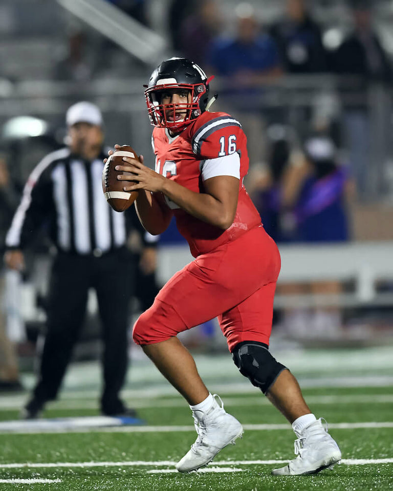 A football player in an red jersey and black helmet, running while holding the ball on field